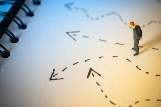 Detailed analysis of a miniature businessman on a printed business plan or strategy diagram, representing mortgage options, lending choices, or financial planning concepts.